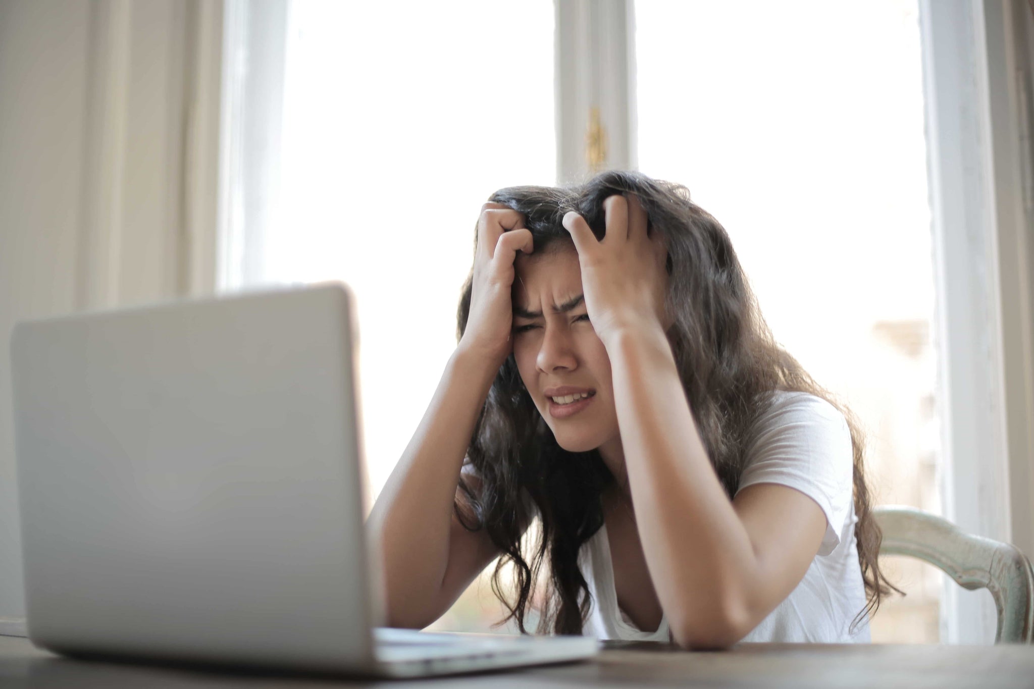 Frau sitzt vor dem Laptop und hält sich beide Hände an den Kopf